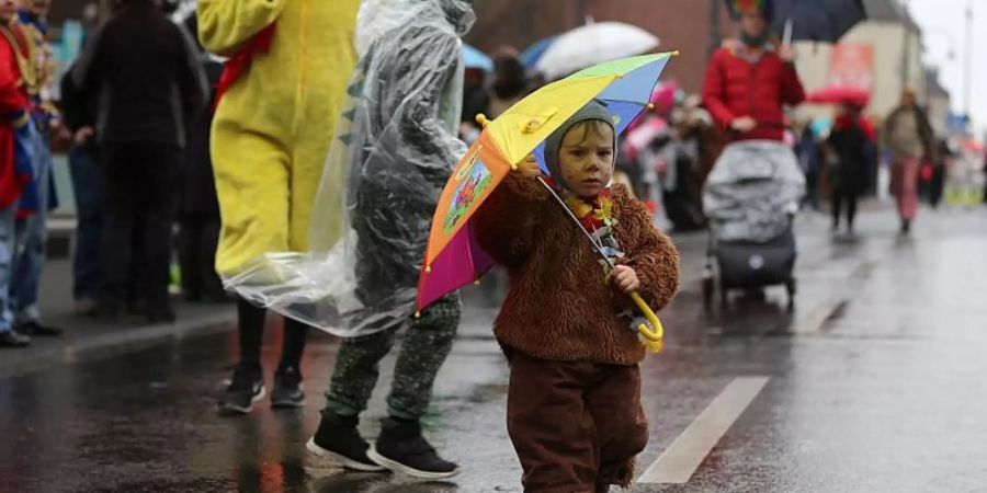 Am Rande der «Schull- un Veedelszöch» geht ein verkleidetes Kind mit Regenschirm über die Strasse. Foto: Oliver Berg