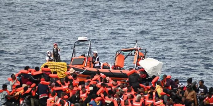 Ein Rettungsboot schwimmt hinter einem völlig überfüllten Flüchtlingsboot. flüchtlingsboot atlantik