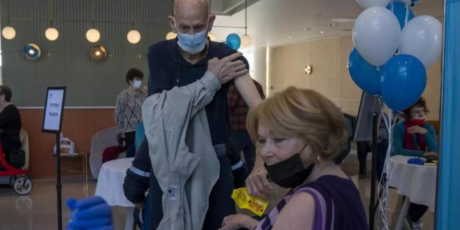 Ein Mann zieht sein Hemd hoch, während seine Frau ihre vierte Dosis des Coronavirus-Impfstoffs in einem privaten Pflegeheim in Petah Tikva erhält. Foto: Ariel Schalit/AP/dpa