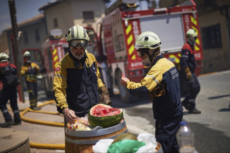 Zwei Feuerwehrmänner unterbrechen den Kampf gegen die Flammen und essen eine Wassermelone, die ihnen von den Einheimischen gegeben wurde.