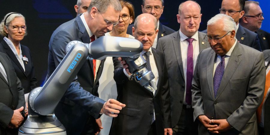 Bundeskanzler Olaf Scholz (M, SPD) und Antonio Costa (r), Premierminister von Portugal, betrachten neben Oliver Jung, Vorstandsvorsitzender Festo beim Eröffnungsrundgang auf der Hannover Messe 2022 einen Roboter mit pneumatischem Antrieb.