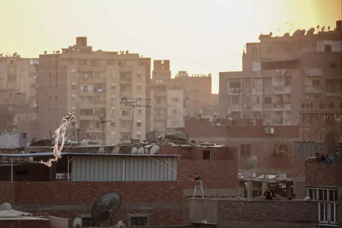 Ein Junge steht auf einem Dach und lässt einen handgefertigten Drachen über Wohnhäuser im Al-Munib-Viertel fliegen. Drachensteigen in Ägypten