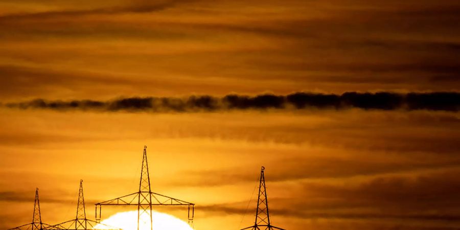 ARCHIV - Die Sonne geht hinter Hochspannungsmasten auf. Foto: Sebastian Gollnow/dpa