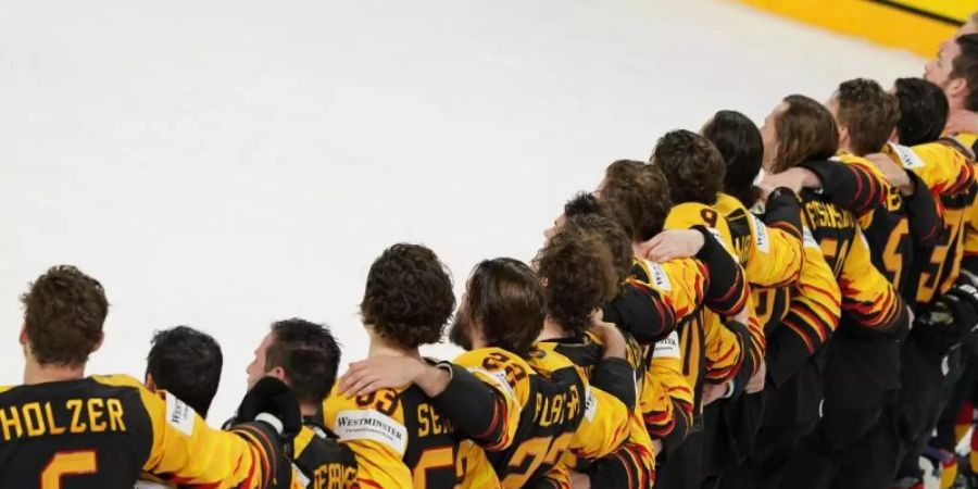 Das deutsche Eishockey-Nationalteam steht Arm in Arm auf dem Eis. Foto: Roman Koksarov/dpa