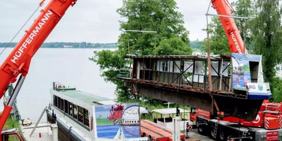 Zwei Mobilkrane heben ein Teilstück des längsseitig zersägten Fahrgastschiffes «MS Oldenburg» am Zwischenahner Meer auf einen Tieflader. Foto: Hauke-Christian Dittrich/dpa