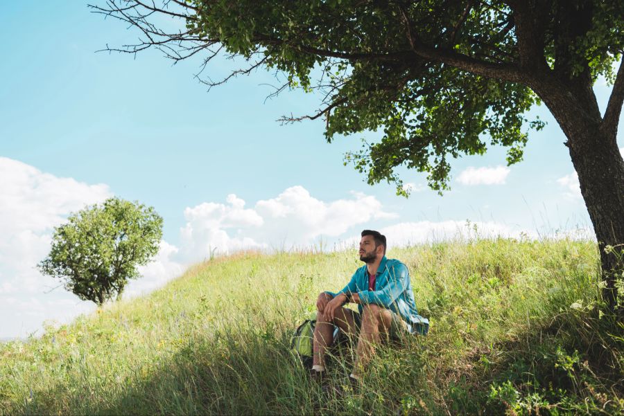 Mann sitzt im Gras unter einem Baum