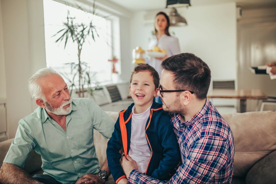 Vater, Sohn und Opa auf einem Sofa, Frau im Hintergrund