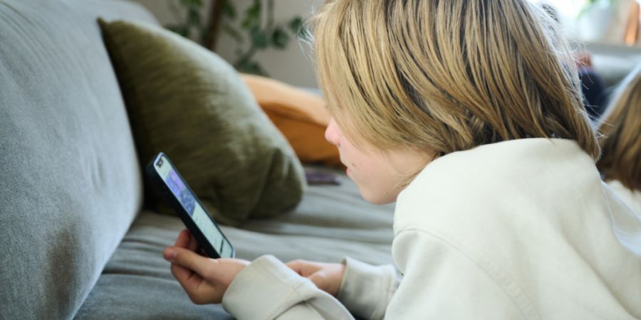 ARCHIV - ILLUSTRATION - Ein Junge liegt auf einem Sofa und guckt auf sein Smartphone. (gestellte Szene). Australien hat ein Social-Media-Verbot für Kinder und Jugendliche unter 16 Jahren eingeführt und ist damit weltweiter Vorreiter. Foto: Annette Riedl/dpa