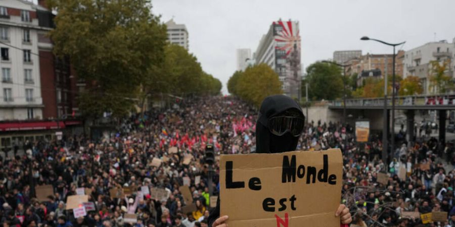 Ein Demonstrant hält während einer Demonstration gegen steigende Lebenshaltungskosten in Paris ein Schild mit der Aufschrift «Die Welt gehört uns» hoch. Foto: Thibault Camus/AP/dpa