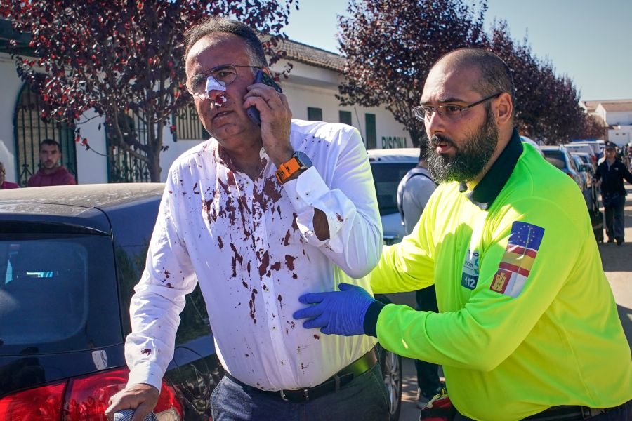 Ein Verletzter mit blutverschmiertem Hemd telefoniert, ein Mitarbeiter des Rettungsdienstes stützt ihn.