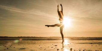 Frau macht am Strand Yoga im Sonnenuntergang.