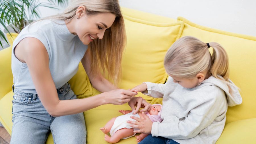 Mutter und Tochter spielen mit Babypuppe