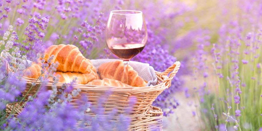 Wein und Croissant vor Lavendellandschaft im Sommer.