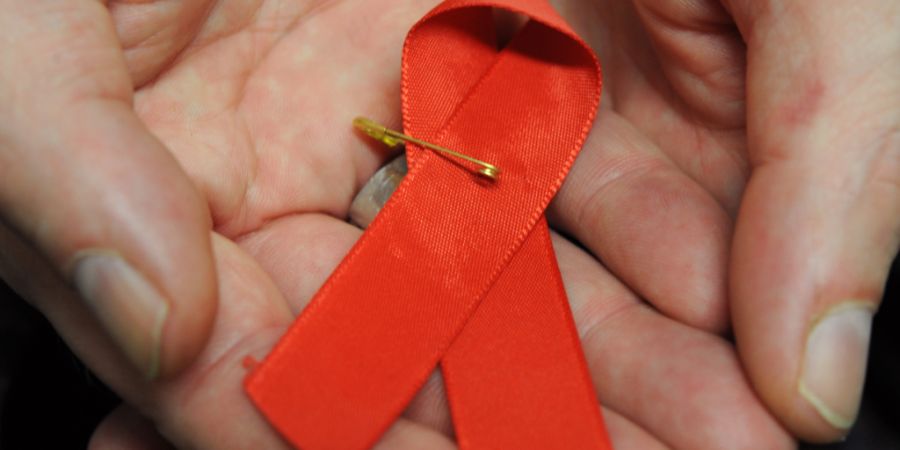 ARCHIV - Ein Mann hält eine rote Schleife als Symbol der Solidarität mit HIV-Positiven und Aids-Kranken. Foto: Arne Dedert/dpa/Archivbild