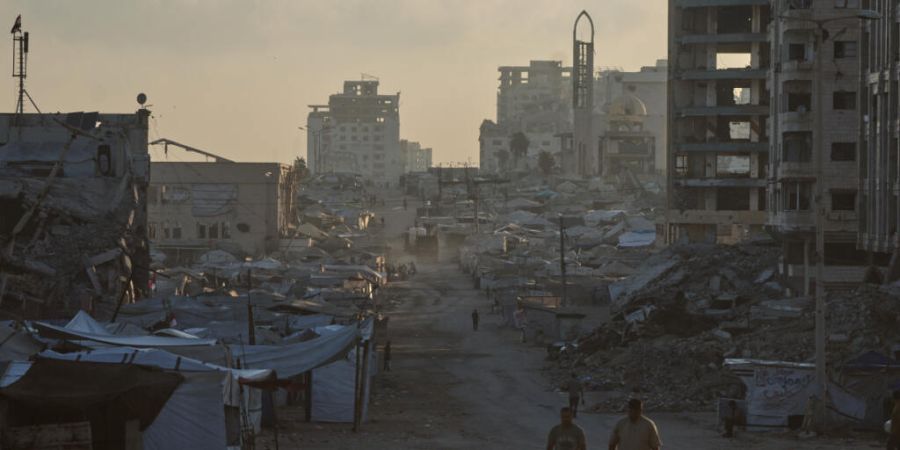 ARCHIV - Palästinenser gehen in Gaza eine Straße entlang, die von Gebäuden gesäumt ist, die bei israelischen Militärangriffen während des Krieges zwischen Israel und der Hamas zer...