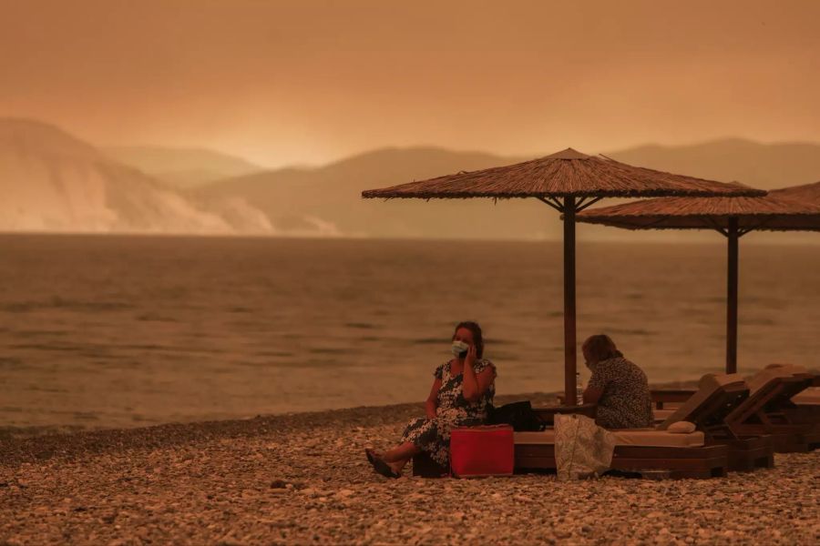 Zwei Menschen sitzen auf einem Strand auf der von Bränden beherrschten griechischen Insel Euböa.