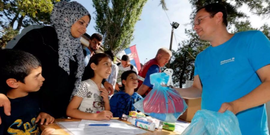 Ein Hilfsarbeiter übergibt einer Flüchtlingsfamilie einen Beutel mit Wasser und Nahrung.