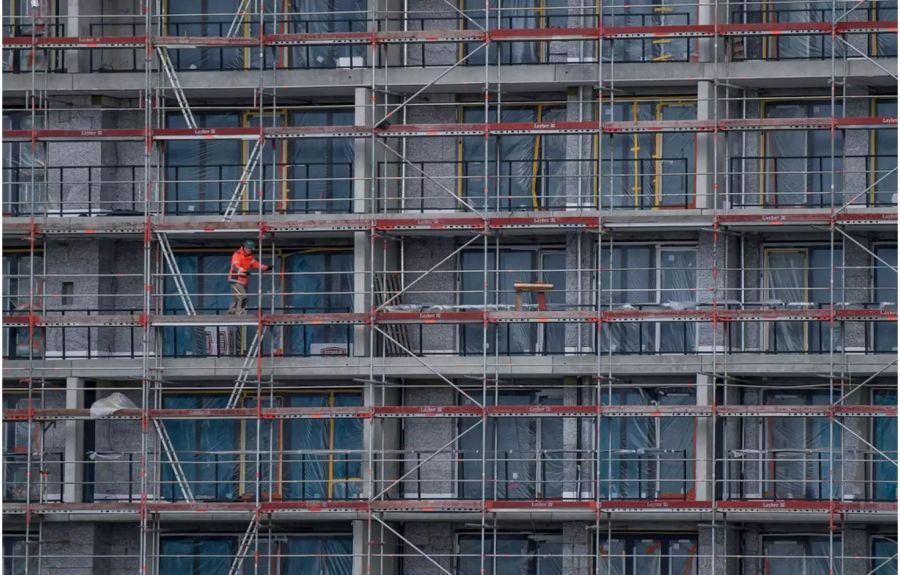 Gebäude in der Bauphase mit Gerüsten und einem Bauarbeiter darauf - Keystone