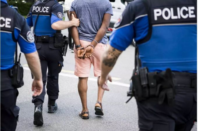 Polizisten laufen mit Mann in Handschellen Richtung Polizeiwagen - Keystone