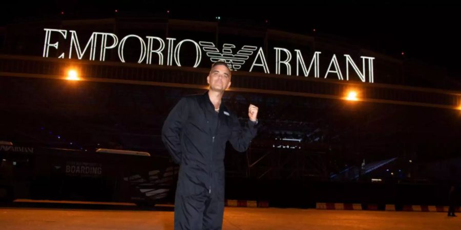 Robbie Williams posiert vor dem Logo von Giorgio Armani.