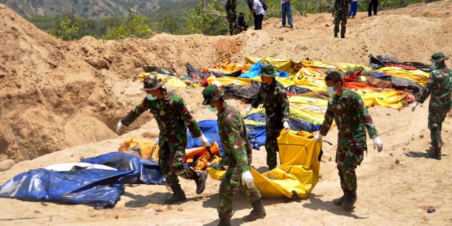 Indonesische Soldaten tragen eine Leiche zu einem Massengrab.