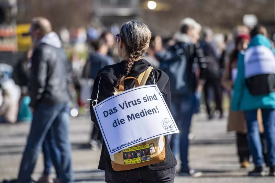 Eine Frau hat ein Schild mit der Aufschrift «Das Virus sind die Medien» umgehängt.