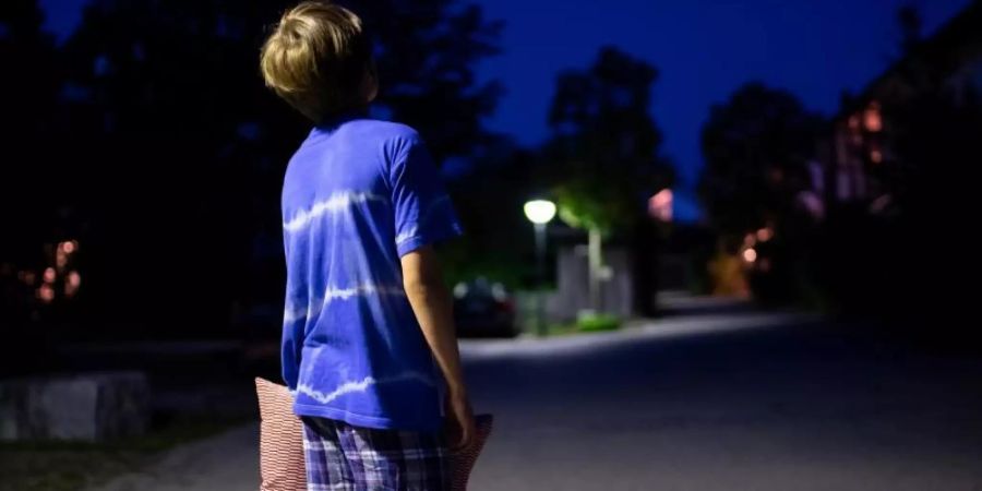 Im Schlafanzug steht ein Kind mit einem Kissen in der Hand nachts auf einer Strasse. Foto: Sven Hoppe/Illustration