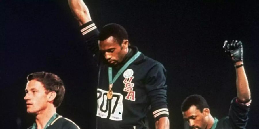 Tommie Smith (M) und John Carlos strecken 1968 bei der Siegerehrung die Fäuste nach oben. Links der australische Silbermedaillengewinner Peter Norman. Foto: Anonymous/AP