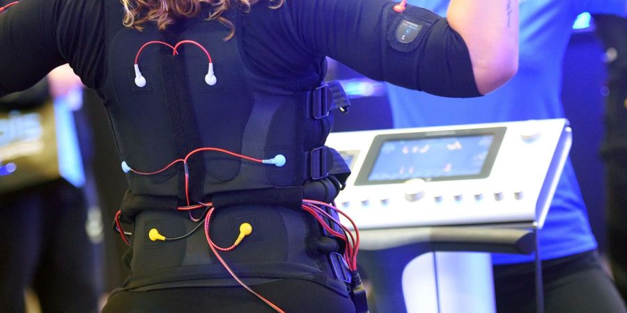 Bei einem EMS-Training trägt man eine verkabelte Weste und Manschetten, über die elektrische Impulse an den Körper weitergeleitet werden.
