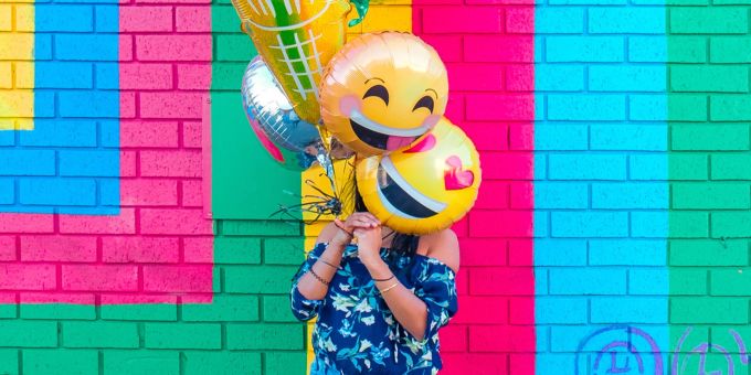 Wer versucht, zwanghaft glücklich zu sein, erreicht damit vielleicht gerade das Gegenteil. Frau mit Smiley Ballonen