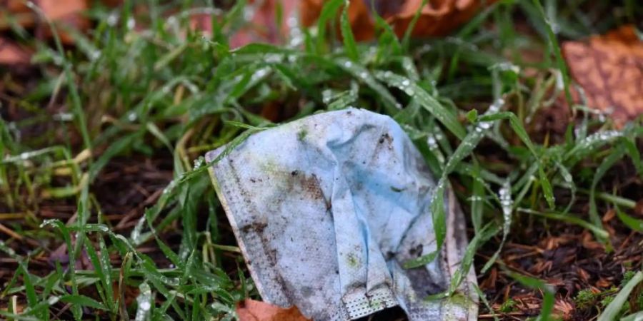 Eine Maske liegt auf einer regennassen Wiese. Corona hat das Leben der Menschen einschneidend beeinflusst. Foto: Robert Michael/dpa-Zentralbild/dpa