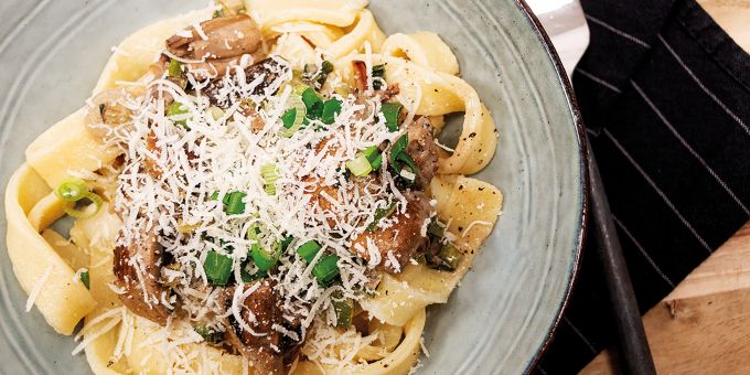 Bei diesem Rezept wird die Kartoffel zur Pasta: luftig leichte Kartoffel-Tagliatelle mit Pilz-Rahm-Sauce. Pasta Pilz Frühlinszwiebel Parmesan Teller Gabel