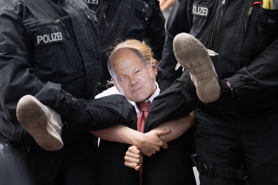 Polizisten tragen eine Anhängerin der «Letzten Generation» mit einer Olaf-Scholz-Maske von einer Strasse in Berlin.