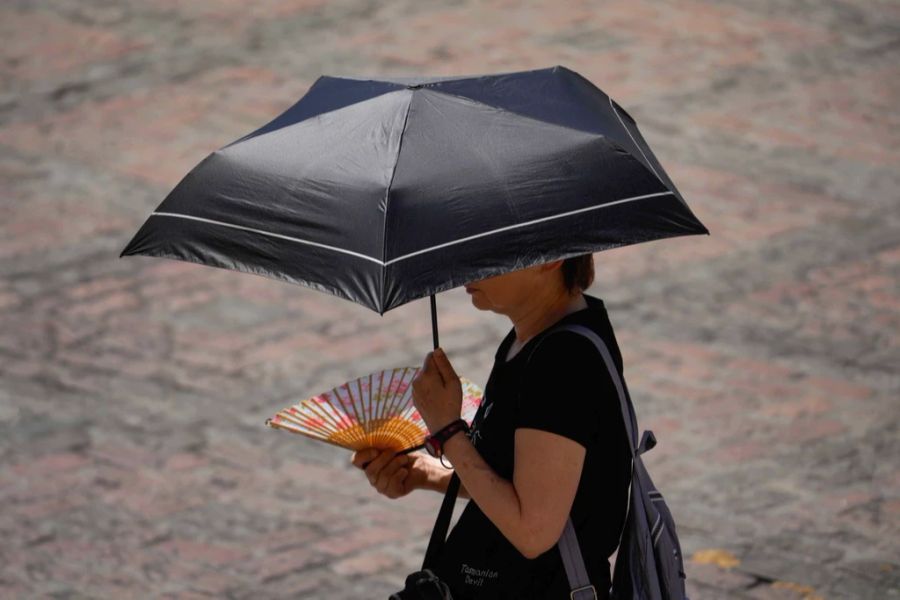 Mit einem Regenschirm und einem Fächer versucht sich eine Spanierin vor der Hitze zu schützen.