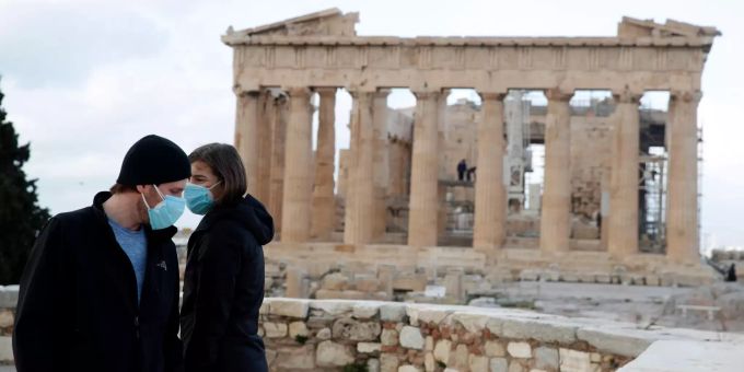 Zwei Besucher stehen mit Mund-Nasen-Schutz vor dem Parthenon-Tempel auf dem Akropolis-Hügel. griechenland