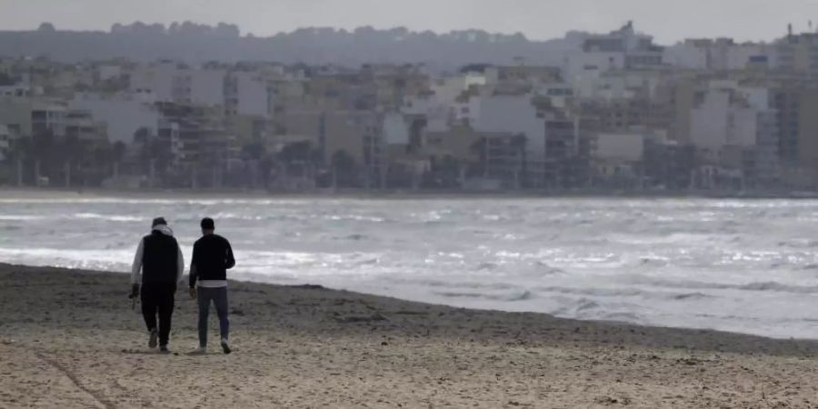 Zwei Männer gehen am Strand von Arenal über den Sand. Foto: Clara Margais/dpa