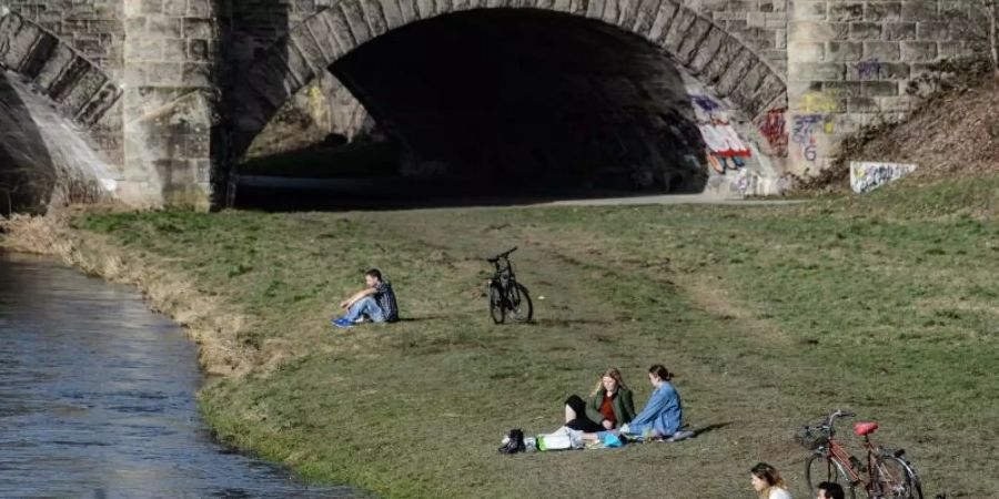 Junge Menschen geniessen am Ufer der Leine in Göttingen das milde Wetter. Foto: Swen Pförtner/dpa