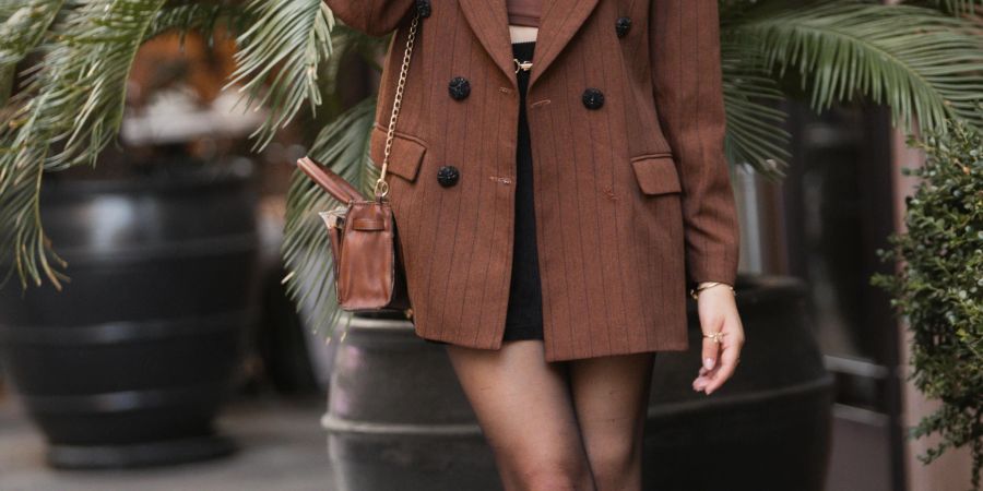 Frau mit braunem Blazer mit dunkler, transparenter Strumpfhose und schwarzen Stiefeletten.