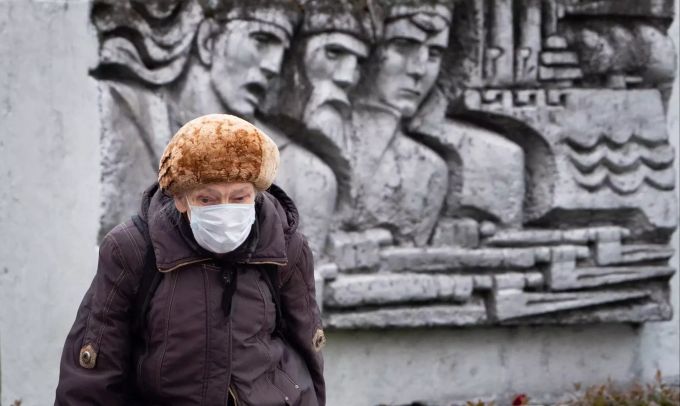 Eine ältere Frau trägt einen Mundschutz als sie an einem Relief aus der Sowjetzeit vorbei geht. Coronavirus - Russland