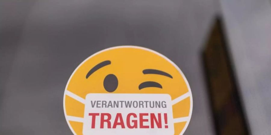 Ein Smiley-Aufkleber "mit Mundschutz" an der Scheibe einer Strassenbahn. Foto: Robert Michael/dpa-Zentralbild/dpa