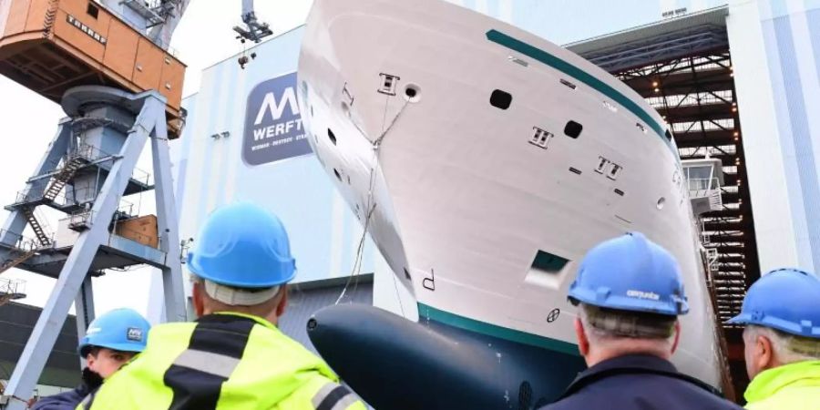 Mitarbeiter beobachten, wie ein Neubau auf der Stralsunder MV Werft eine Schiffbauhalle verlässt. Foto: Stefan Sauer/dpa-Zentralbild/dpa