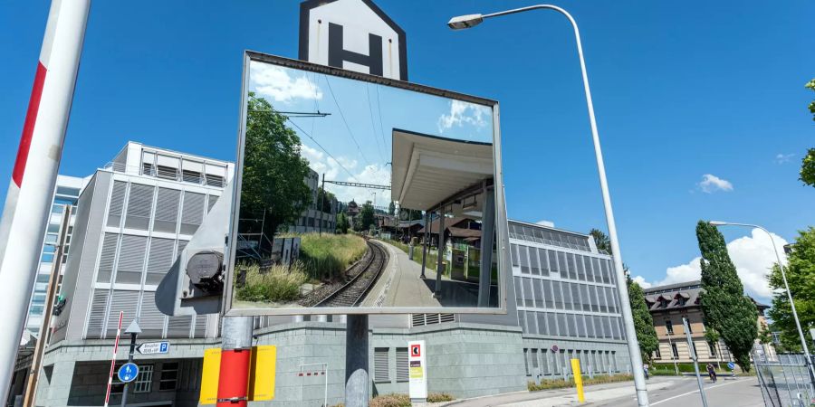 BLS Bahnhof Liebefeld und einspurige Bahnlinie in Richtung Köniz und Schwarzenburg durch einen Spiegel gesehen. Im Hintergrund das Betriebsgebäude der Berner Kantonalbank (BEKB) an der Schwarzenburgstrasse 160 in Liebefeld.