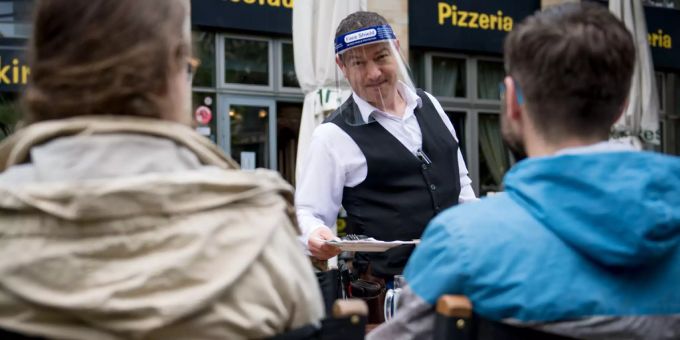 Ein Serviceangestellter schützt sich mit einem Plastikvisier vor einer Corona-Ansteckung.