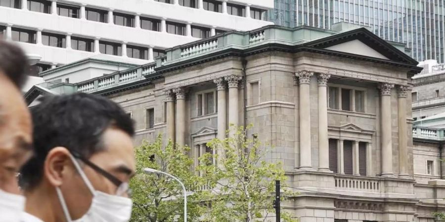 Menschen gehen mit Gesichtsmasken am Gebäude des Hauptsitzes der «Bank of Japan» (BoJ) in Tokio vorbei. Foto: Shinji Kita/Kyodo News/AP/dpa