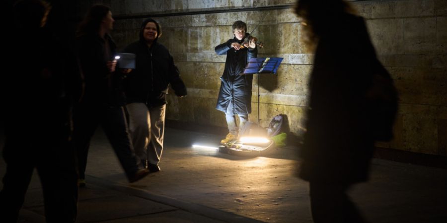 ARCHIV - Ein Straßenmusiker spielt Geige, während Menschen in einer U-Bahn-Querung während der Verdunkelungszeiten aufgrund der regelmäßigen russischen Luftangriffe in der ukrainis...