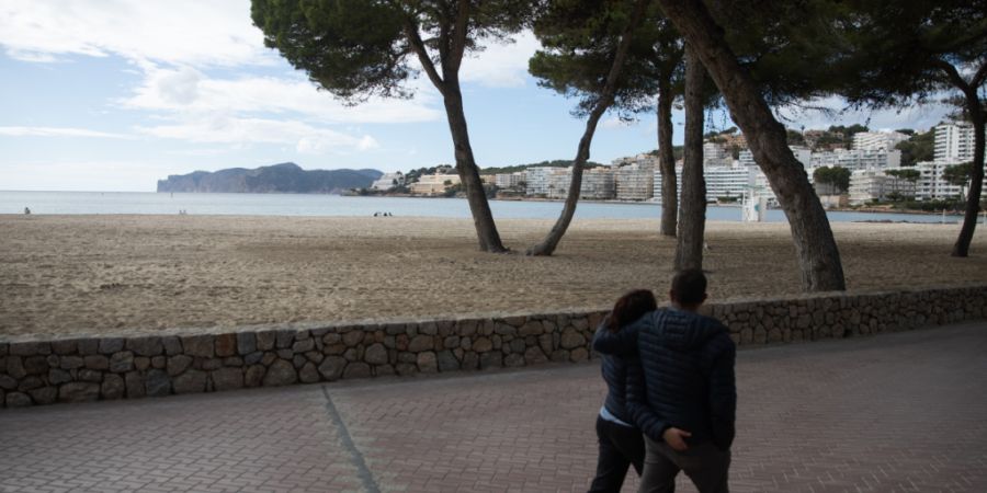 ARCHIV - Menschen spazieren am Strand von Santa Ponça auf Mallorca am Meer entlang. Foto: Clara Margais/dpa