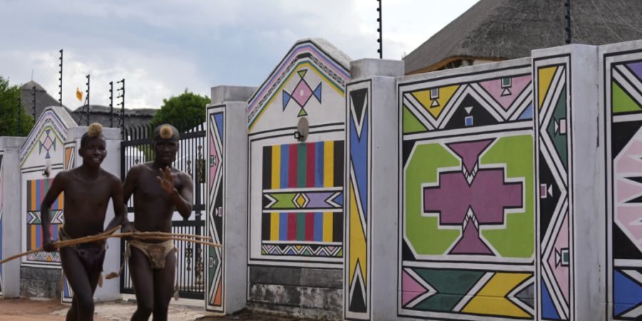 ARCHIV - Junge Männer vom Volk der Ndebele laufen am Haus von Esther Mahlangu, einer zeitgenössischen südafrikanischen Künstlerin, in KwaMhlanga in Mpumalanga, Südafrika, vorbei. F...