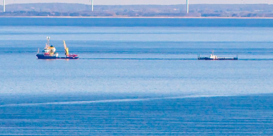 dpatopbilder - Ein Schiff zieht vor Fehmarn die Barge mit dem gestrandetem Wal. Im Hintergrund ist die dänische Küste zu sehen. Foto: Bodo Marks/dpa