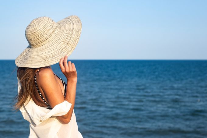 Auch Hüte schützen vor schädlicher Sonnenstrahlung. Frau mit Hut am Meer