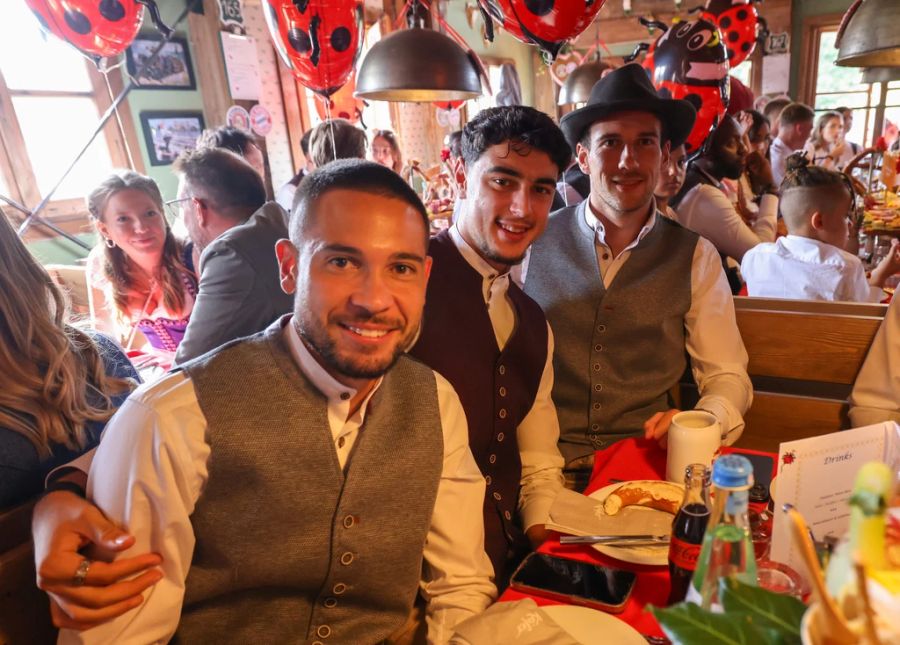 Raphael Guerreiro, Aleksandar Pavlovic und Leon Goretzka sitzen im Festzelt.